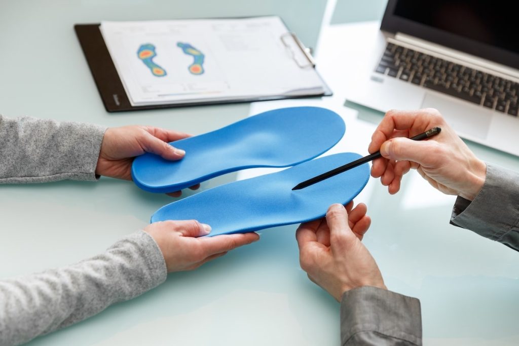Custom Orthotic Insoles Being Measured And Examined On A Glass Desk With A Laptop And Foot Analysis Chart.