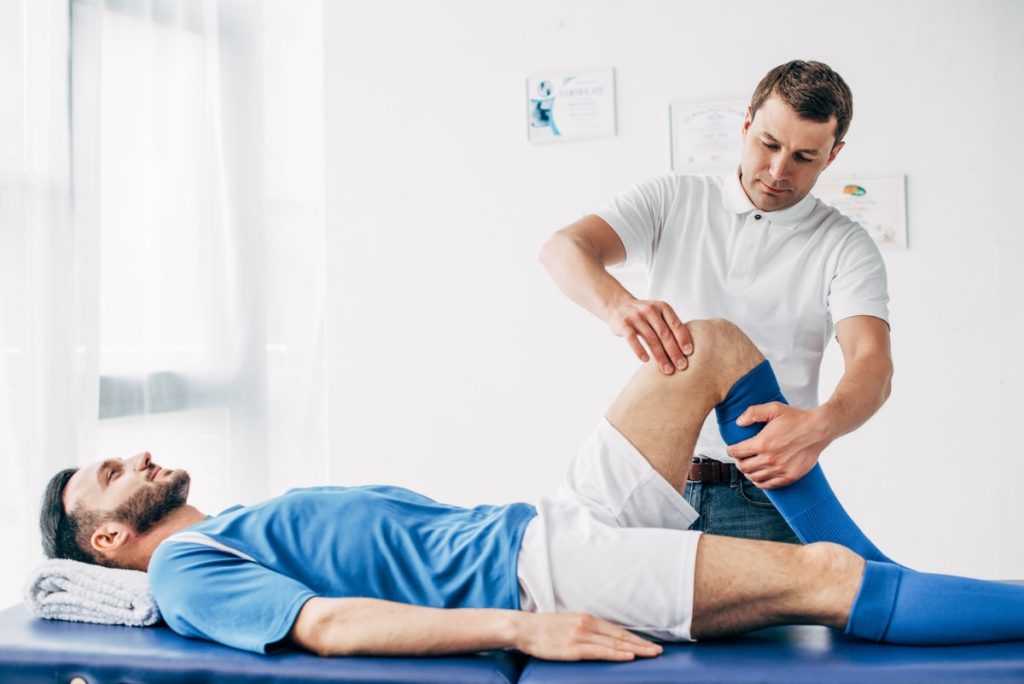 Physical Therapist Assisting A Soccer Player With Leg Exercises In A Sports Medicine Clinic.
