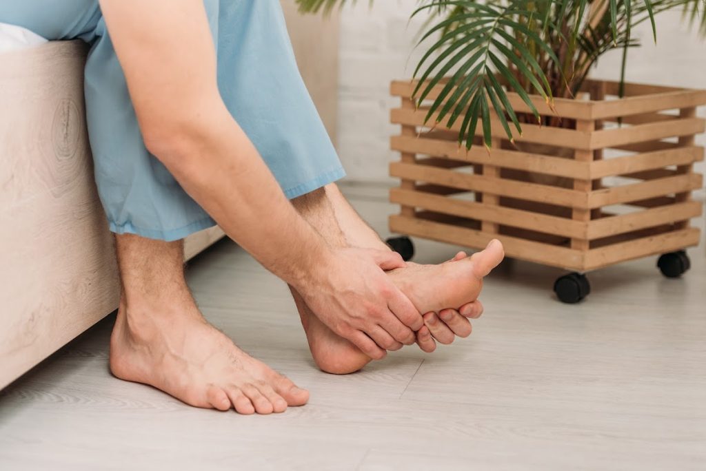 Man Sitting And Holding His Foot, Suggesting Foot Discomfort.
