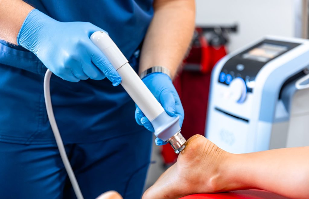 Technician Administering Acoustic Shock Wave Therapy On Patient's Foot In Clinic Setting.